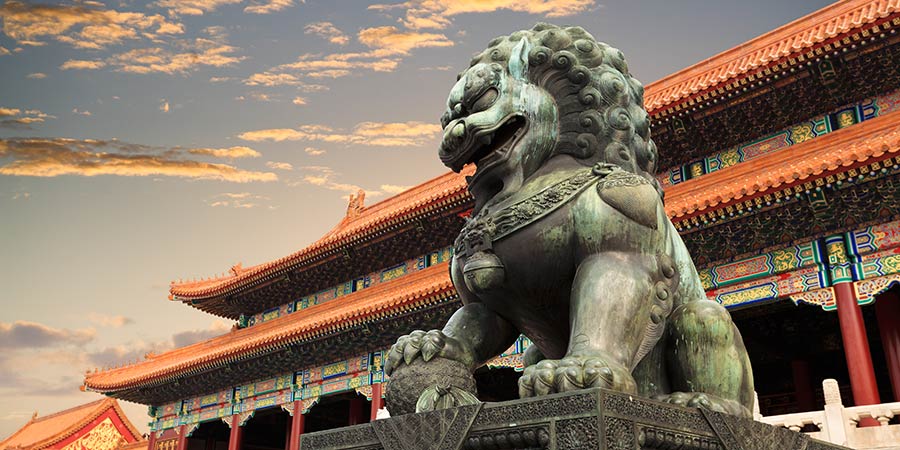 A large metal statue of a traditional Chinese lion stands in front of the Forbidden City’s dramatic gates.  